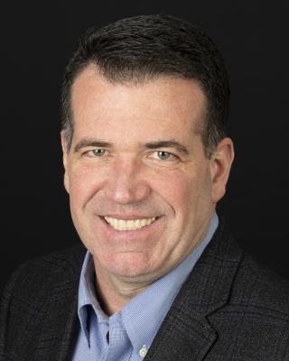 a man wearing a suit and tie smiling and looking at the camera