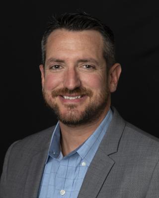 Jake Sutton wearing a suit and tie smiling and looking at the camera